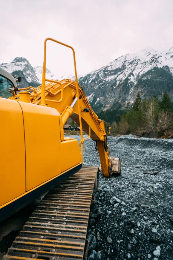 side view close up shot of excavator with snow capped mountains in the distance