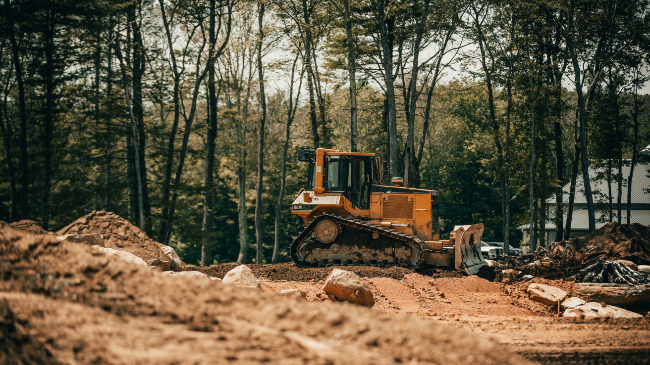 ACP Hauling & Excavation's bulldozer works amidst a future home site, meticulously crafting a clean slate for dream home foundations against a forest backdrop.
