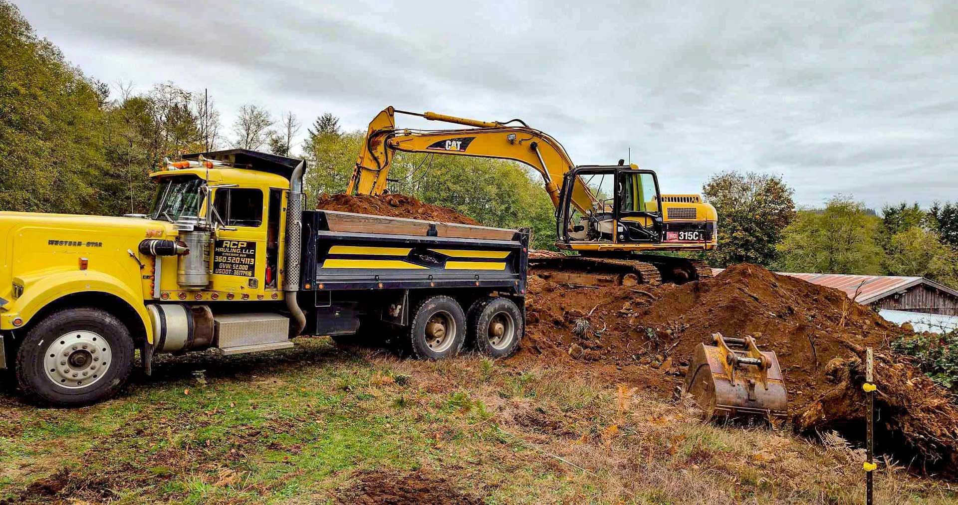 ACP Hauling & Excavation's vibrant yellow truck being loaded with fill dirt by a powerful CAT excavator, a symbol of industrious synergy at the heart of a construction site.
